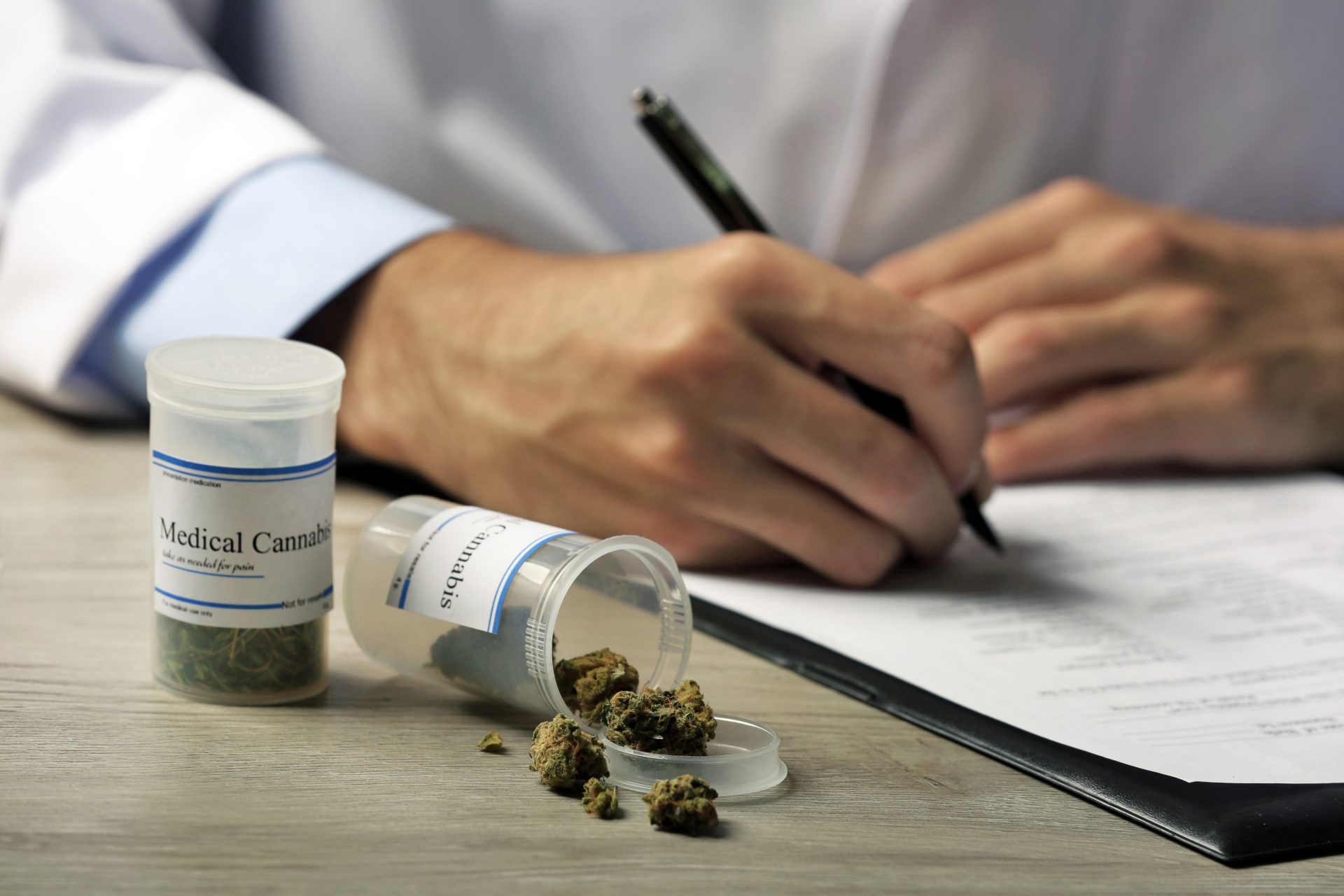 closeup of medical practitioner's hand writing on a paper beside a cannabis container