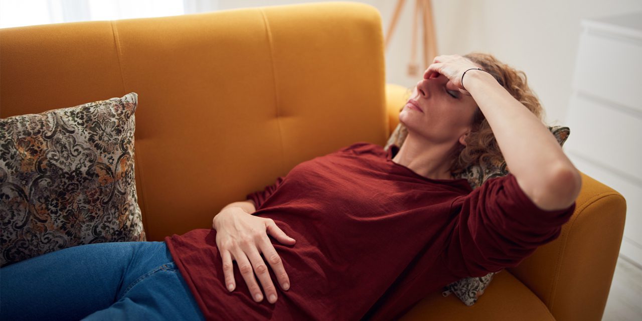 woman lying on a sofa holding her forehead