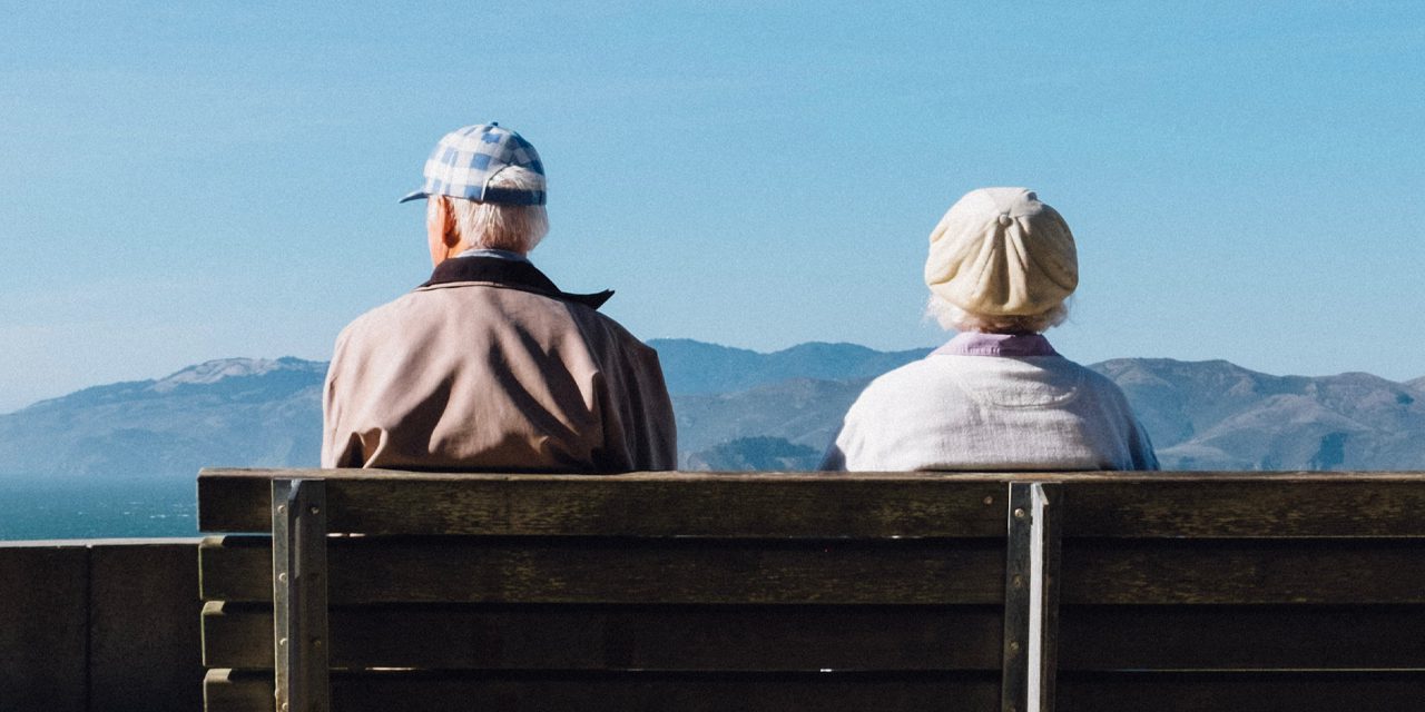 old man and woman sitting next to each other in bench fronting a mountain view
