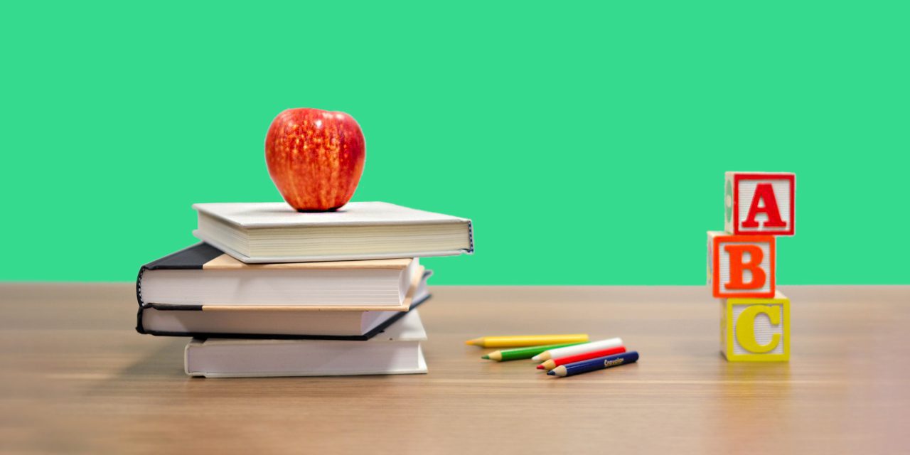 compiled books with apple on top, color pencils and ABC blocks