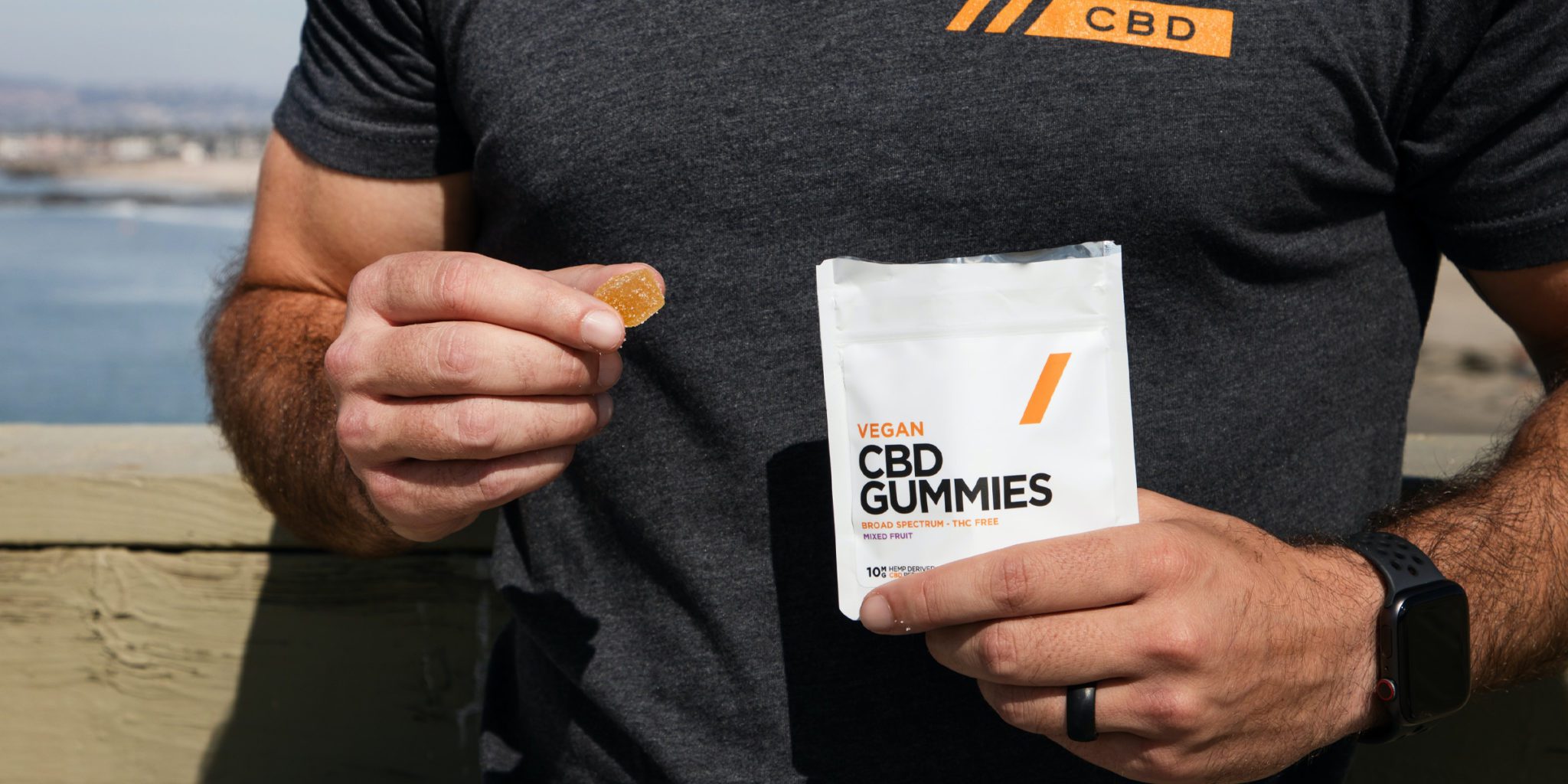 closeup of man's hand holding CBD gummies, one gummy on the right hand and pack of gummies on the other hand