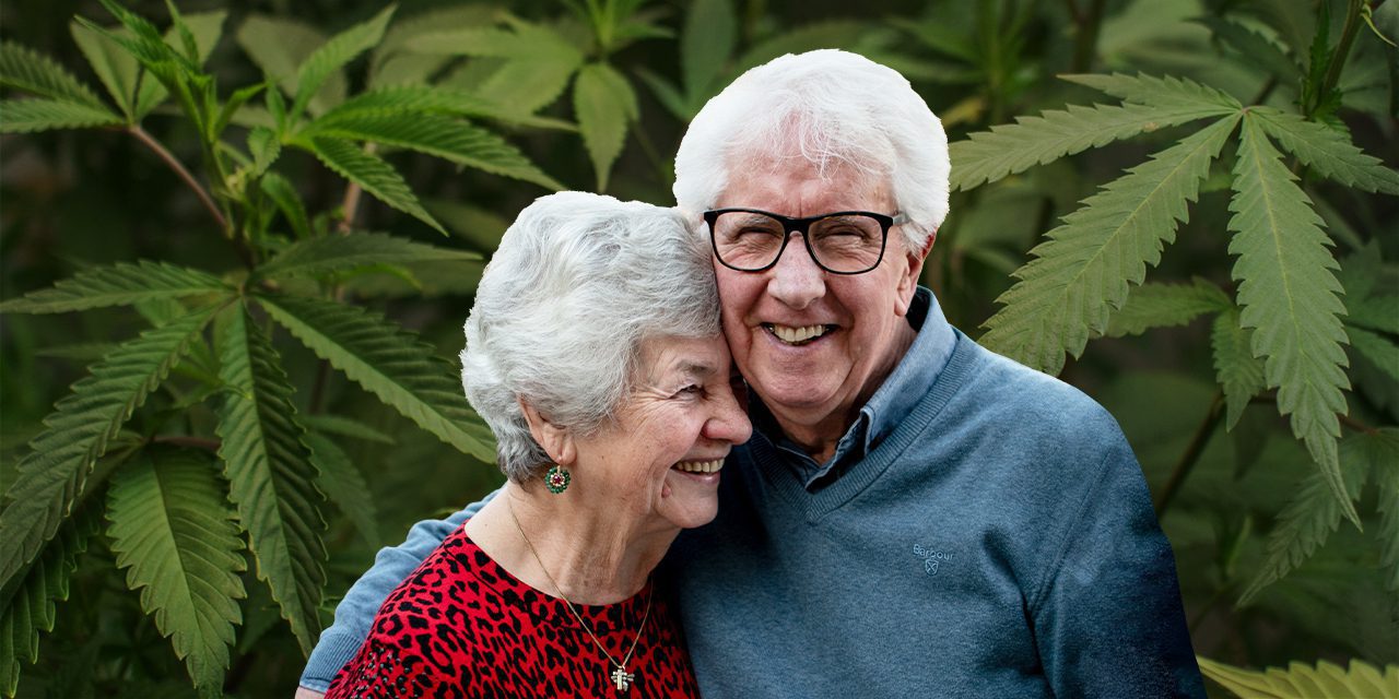 una pareja de ancianos felices con una planta de cannabis de fondo