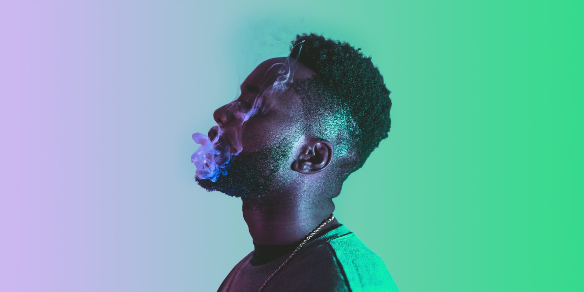 closeup photo of black man blows smoke out of his mouth in a purple green gradient background