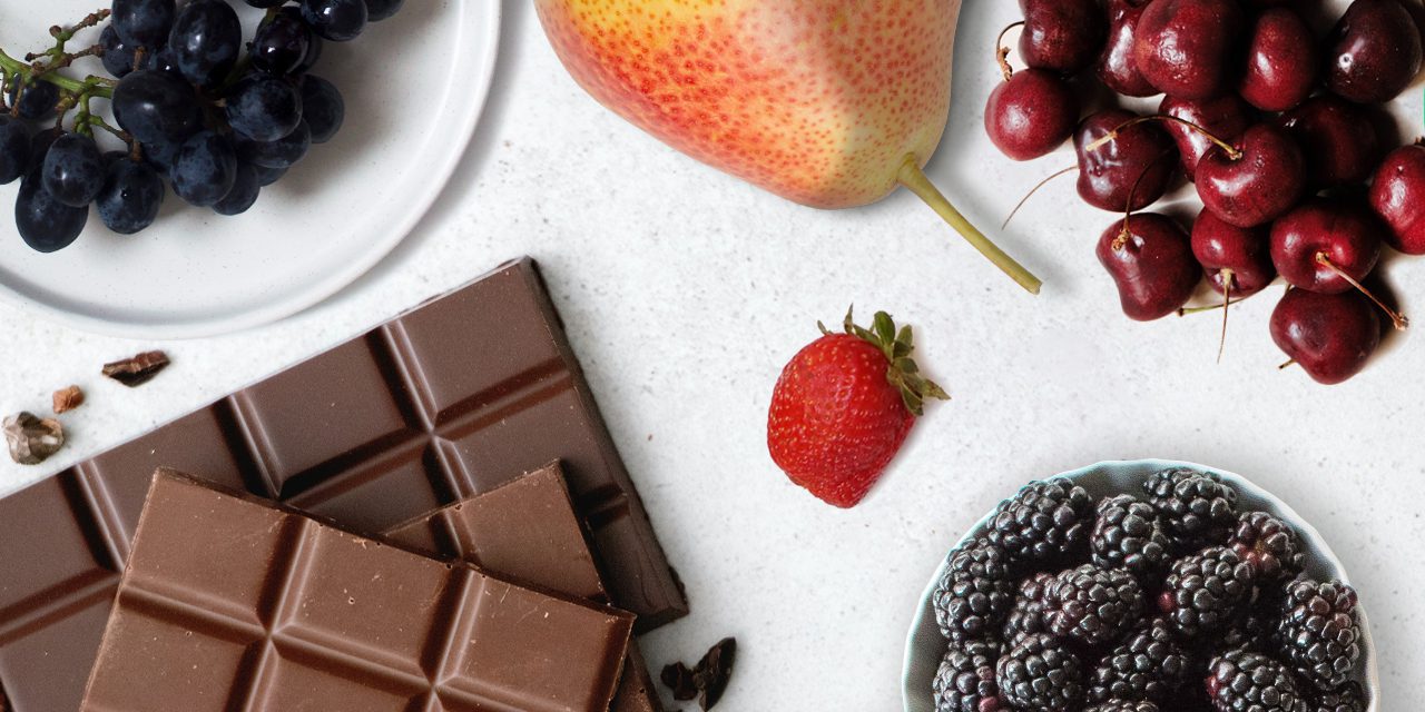 varieties of fruits, plate of black grapes, pear, cherries, small plate of blackberries, a strawberry and bars of chocolate