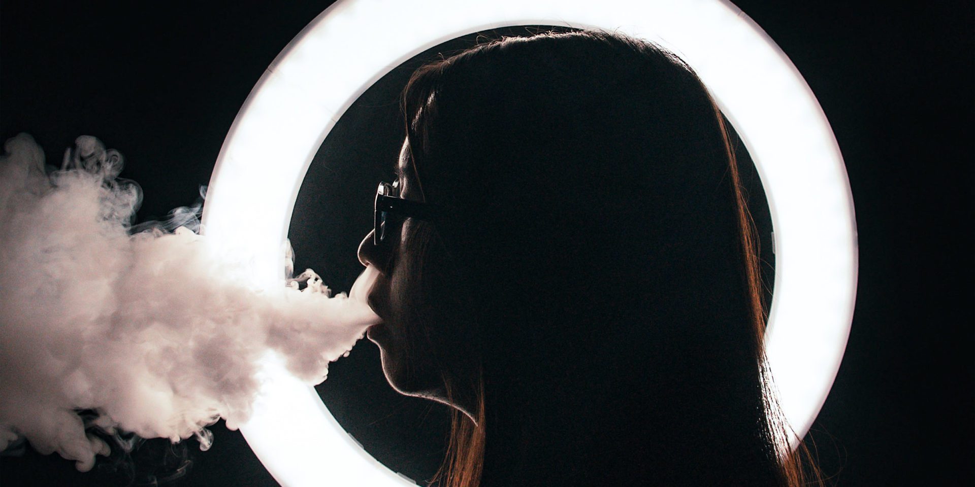 a woman wearing eyeglasses, blowing smokes outside the mouth