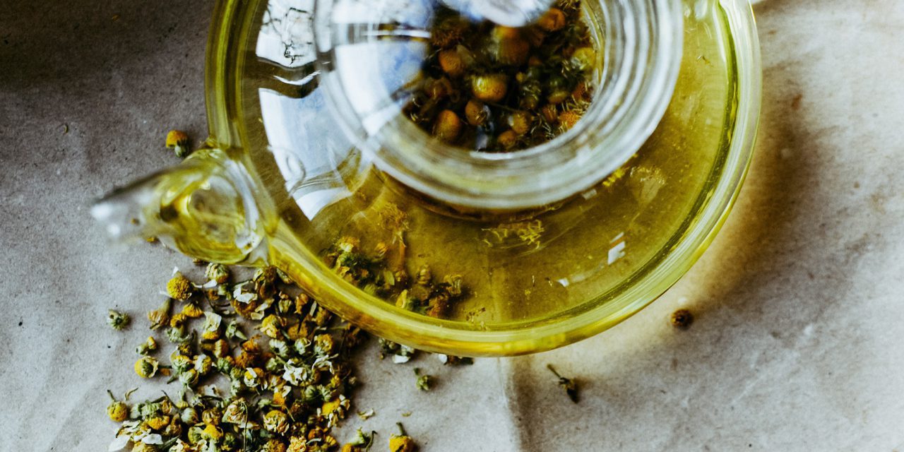 top view of glass tea pot with dried chamomile flowers outside and inside the tea