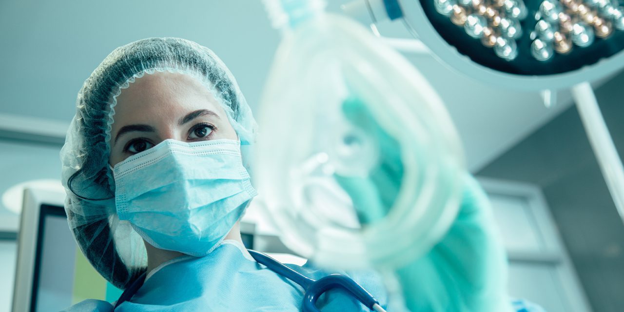 a medical practitioner/staff on her blue surgical cap, gown and mask inside operating room