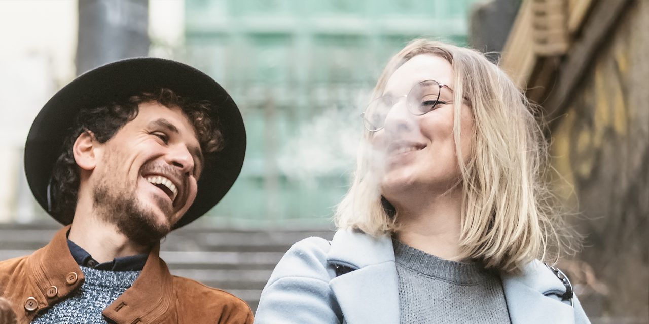 man and woman laughing together while a woman blowing off a smoke from her mouth