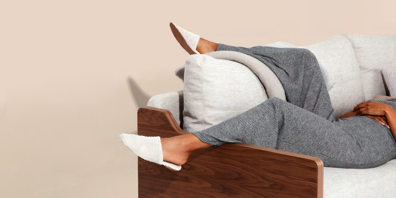 woman lying on couch placing one leg above the couch's pillow while other leg hanging on the end