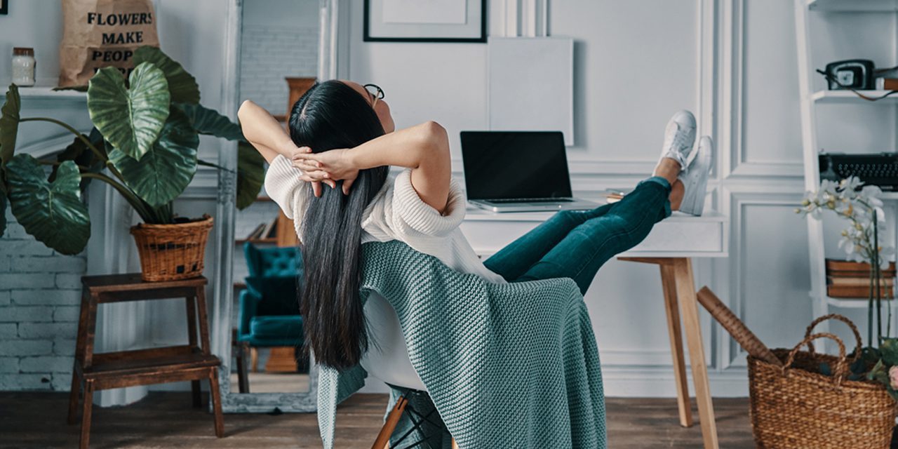 woman sitting in a chair while raising her legs over her desk and crossing her hands over her head