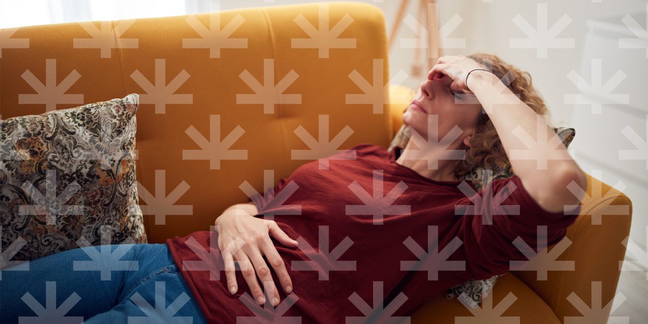 woman lying on sofa touching the middle of her nose and other hand lies on stomach