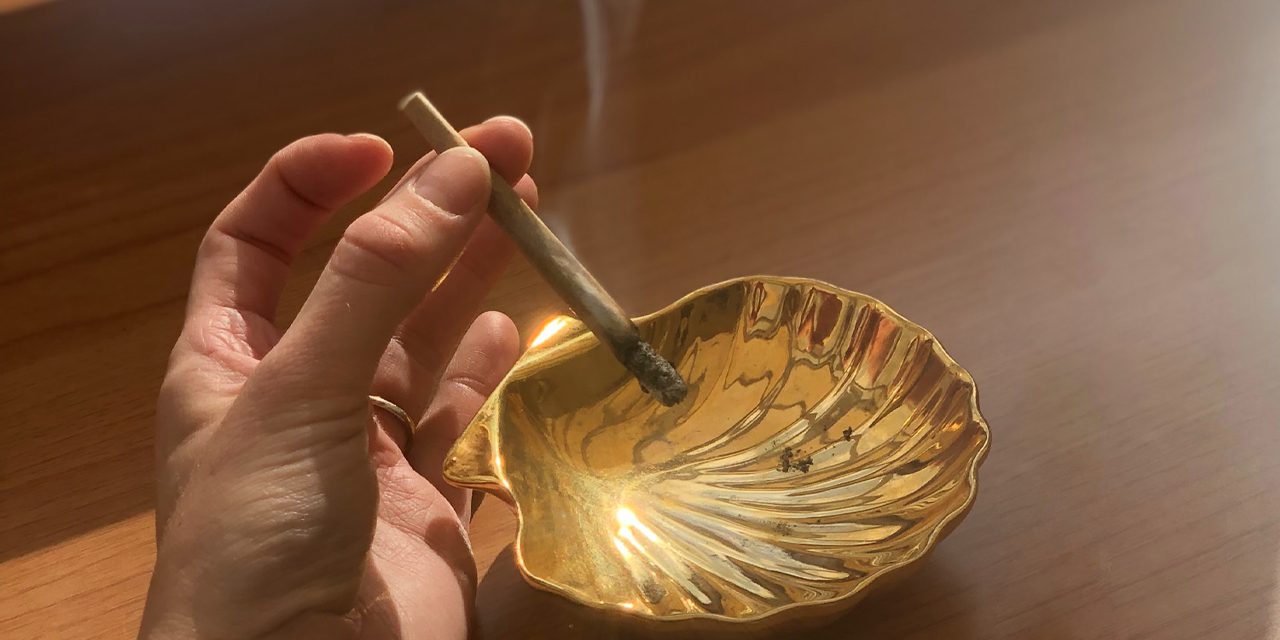 closeup of hand holding smoking rolled weed over clamp shaped ashtray